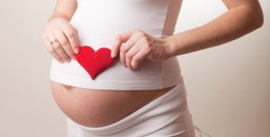 pregnant woman put a toy heart to his stomach